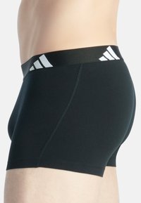 Svarta boxerkalsonger i mjuk tyg med en kontrasterande vit adidas-logotyp på den mjuka linningen. Tätt sittande design.