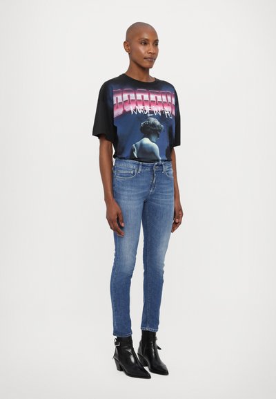 Svart grafisk t-skjorte med blå og rosa trykk, kombinert med lyseblå skinny jeans og svarte ankelstøvler med spiss tå.