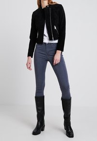 Svart suéjacka med asymmetrisk dragkedja, tillsammans med grå skinny jeans och knähöga svarta läderstövlar. Minimalistisk design, mjuk textur.