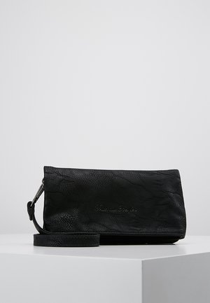 Pochette bracelet en cuir noir texturé avec bandoulière détachable, forme rectangulaire, et nom de marque discrètement embossé sur le devant.