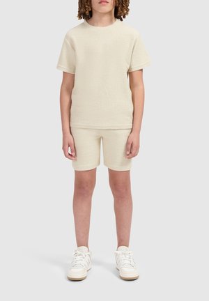 Lichtbeige twee-delige outfit bestaande uit een textuur shirt met korte mouwen en bijpassende shorts, gecombineerd met witte sneakers.