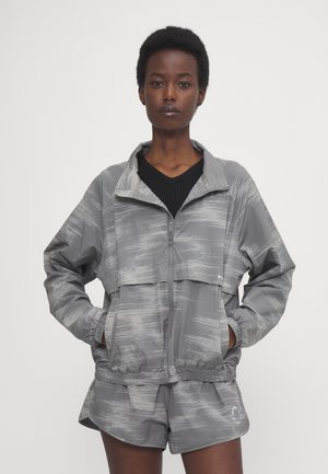 Giacca sportiva grigia con un design a trama, chiusura con zip e vita elastica, abbinata a pantaloni corti coordinati con un motivo simile.