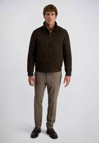 Braune Wildlederjacke mit hohem Kragen, Frontreißverschluss und gerippten Bündchen, kombiniert mit hellbraunen, plissierten Hosen und dunklen Loafers.