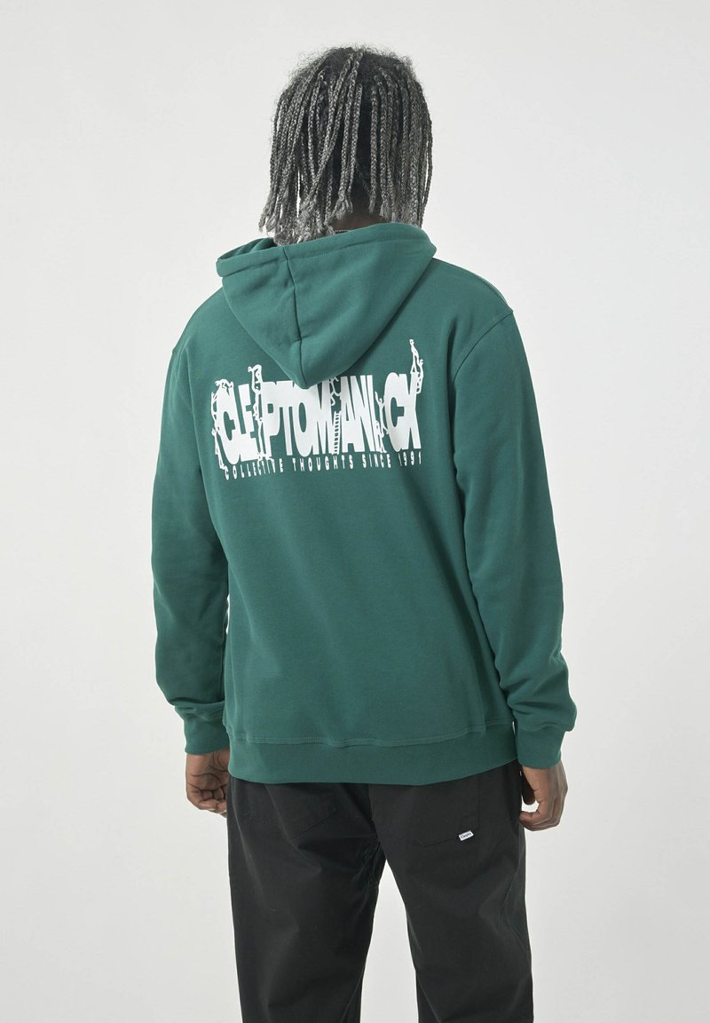 Green hoodie with a drawstring and kangaroo pocket, featuring a large white graphic text on the back. Paired with black pants.