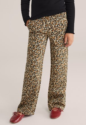 Beige wijde broek met luipaardprint en bruine en zwarte vlekken. Lichtgewicht stof met zijzakken. Gecombineerd met rode schoenen.