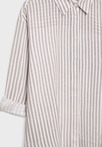 Koszula z kołnierzykiem zapinana na guziki z pionowymi beżowo-białymi paskami, długie rękawy podwinięte, wykonana z lekkiego materiału.