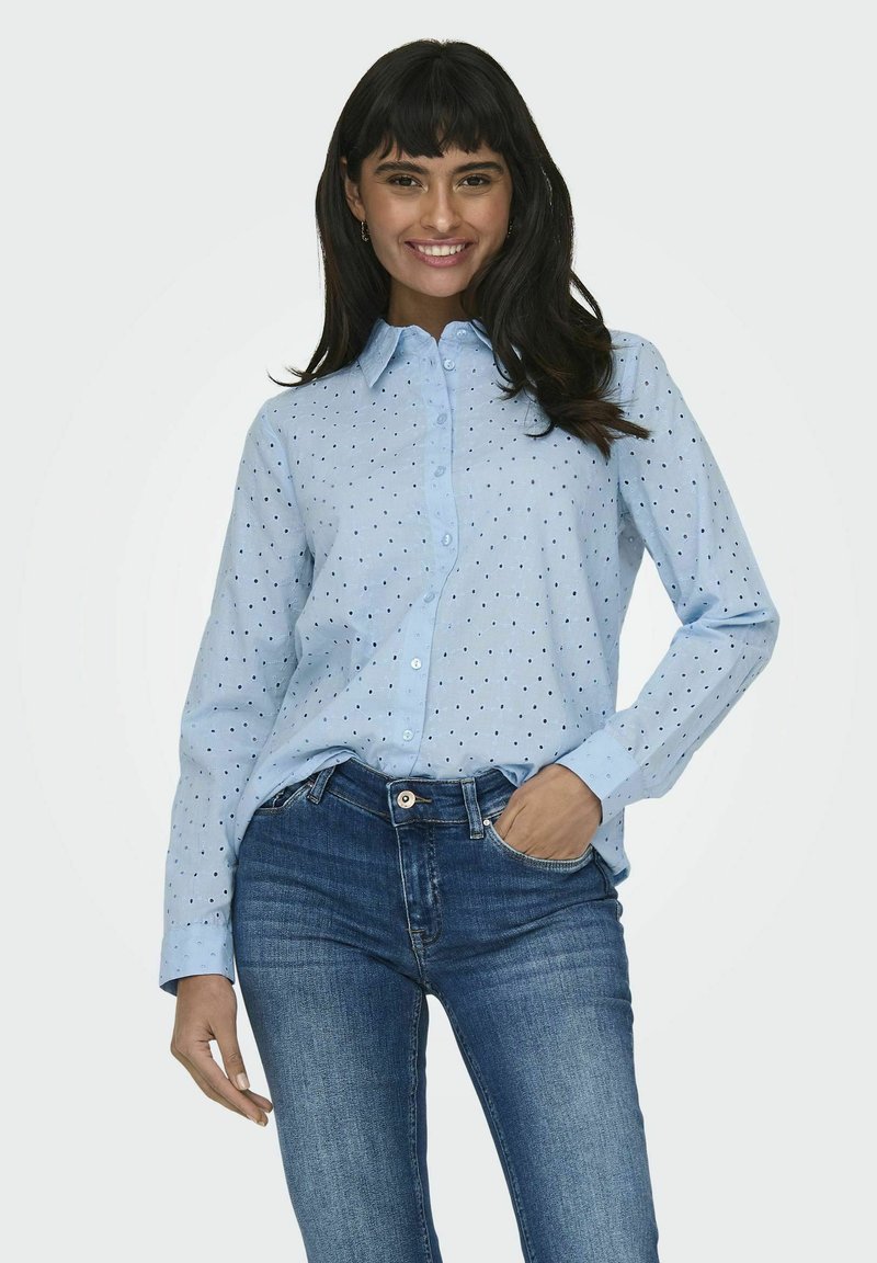 Camicia azzurro chiaro con pois neri, a maniche lunghe e colletto a punta, abbinata a jeans fitted blu scuro.