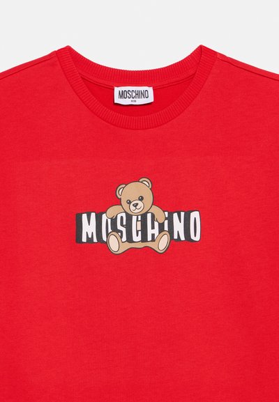 Κόκκινο βαμβακερό μπλουζάκι με κεντρικό γραφικό ενός αρκούδου και το κείμενο «MOSCHINO» σε έντονα μαύρα και λευκά γράμματα. Σχεδιασμός με στρογγυλή λαιμόκοψη.