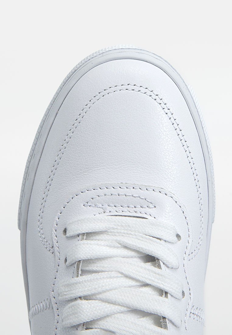 Weiße Leder-Sneaker mit glatter Textur, abgerundetem Zeh, flachen weißen Schnürsenkeln und genähten Details entlang der Kanten. Einfaches Design ohne Muster.