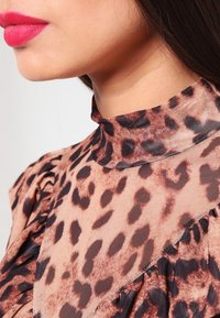 Leopard print blouse with a high neck, ruched details, and a sheer, lightweight fabric in tones of tan and brown.