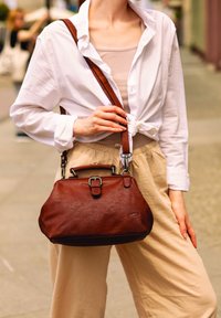 Bruine leren handtas met een gestructureerde vorm, contrasterende donkerdere onderkant, een bovenhandvat en een verstelbare schouderriem, met metalen accenten.