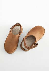 Chaussures en suédine marron avec un intérieur doux et moelleux, bout rond et détail de sangle sur le côté. Semelle plate et talon arrondi pour le confort et la facilité.