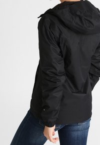 Svart vattentät jacka med huva, utrustad med elastiska muddar och en figursydd design. Materialet har en slät textur utan synliga mönster.