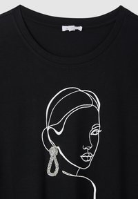 Czarny t-shirt z białym rysunkiem twarzy. Zawiera błyszczący, ozdobny element w postaci kolczyka po prawej stronie.