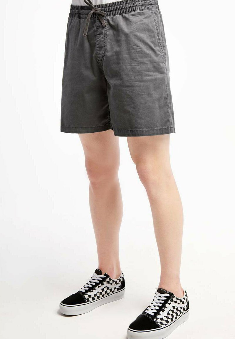 Grijze katoenen shorts met een elastische taille en een trekkoord. Beschikt over zijzakken en een losse fit. Gecombineerd met zwart geruite sneakers.
