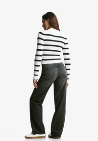 Maglione a righe, in maglia a coste, bianco e nero, abbinato a jeans grigi a vita alta e a gamba larga. Il modello indossa sneakers bianche.