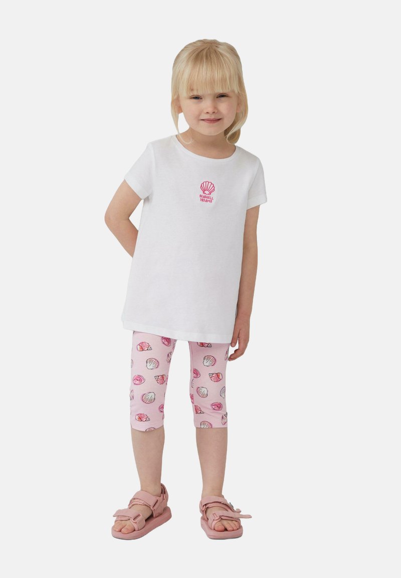 Witte T-shirt met een roze schelpprint en de woorden "SEASIDE DREAMS", gecombineerd met roze leggings met een schelpdesign. Roze sandalen.