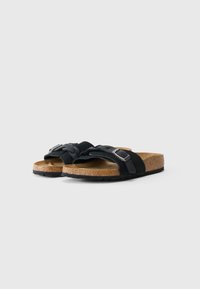 Sandales à glisser en suède noir avec un design de sangle tissée, accent de boucle en métal, semelle en liège et semelle en caoutchouc texturé.