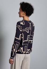 Camicia a maniche lunghe di colore blu scuro con motivo astratto beige; presenta una vestibilità comoda e un orlo elastico per un leggero effetto bluson.