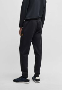 Svart atletisk joggers med ribbad midja, muddar och en liten logopatch på sidan, tillverkad av en mjuk, texturerad tyg.