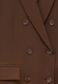 Brown double-breasted blazer made from smooth fabric featuring six round buttons, a pocket flap, and sharp lapels.