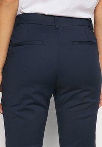 Pantaloni blu navy su misura realizzati in tessuto morbido, dotati di due tasche posteriori e un design aderente con vita a media altezza.
