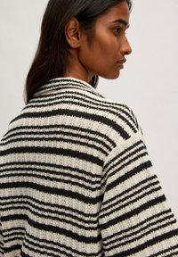 Gestreifter Cardigan in Schwarz und Creme. Strickstruktur mit lockerer Passform, weit geschnittenen Ärmeln und einem Kragen im Rücken.