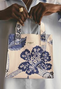 Neliela baltā rokassoma ar zilām ziedu motīvu, kurai ir izturīgas rokturi un logotipa birka. Izgatavota no izturīga materiāla ar gludu tekstūru.