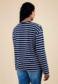 Camisa de manga larga a rayas azul marino y blanca, con escote redondo y un corte holgado, combinada con jeans de un azul claro. Textura de tela suave.