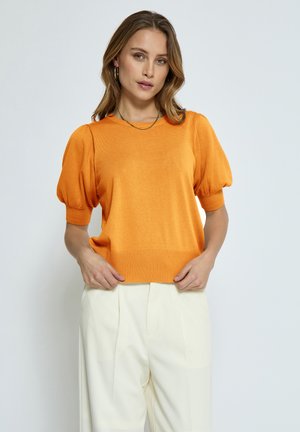 Orange puffärmad tröja med ribbad fåll och halsringning. Bärs med ljusa, veckade byxor. Mjuk textur, avslappnad passform.