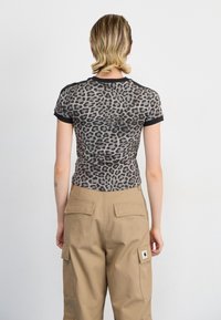 Průhledný top s leopardím potiskem a krátkými rukávy, obohacený o černé lemy, spárovaný s khaki cargo kalhotami s zadními kapsami a značkovým štítkem.