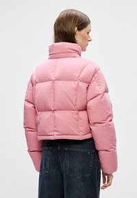 Roosa puffer jakk, millel on lühike disain, kõrge krae ja tikitud osad. Materjal näib olevat sile ja pehmendav soojuse jaoks.