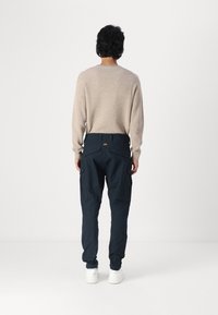 Pulover tricotat bej cu o croială clasică, combinat cu pantaloni cargo navy cu buzunare laterale și un talie texturată, purtat cu adidași albi.