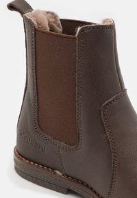 Hnědá kožená kotníková bota s elastickým bočním panelem, měkkou vnitřní podšívkou a kontrastními texturovanými detaily u podešve a holenní části.