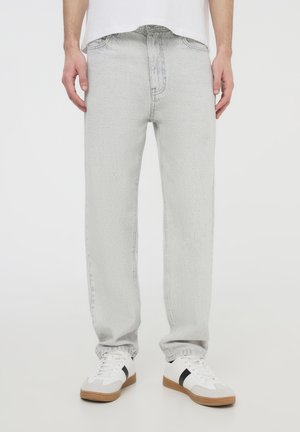 Jeans di denim grigio chiaro con una vestibilità dritta, caratterizzati da una superficie texturizzata, un design a cinque tasche e un aspetto usurato. Indossati con sneakers bianche.