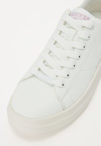 Weiße Schnürsneaker mit einem glatten synthetischen Obermaterial, runder Zehenpartie und einer Gummisohle. Enthält ein dezentes „Guess“-Logo in Hellblau.