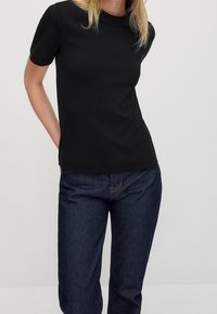 Svart t-shirt med kort ärm gjord av slätt material; har en rund halsringning och en figurnära design, kombinerad med mörkblå jeans.