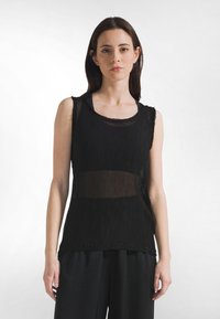 Czarny bezrękawnik z teksturowanym, plisowanym wzorem. Posiada zaokrąglony dekolt i przezroczyste elementy, zestawiony z luźnymi czarnymi spodniami.