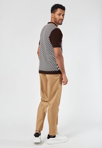 Short-sleeve polo in brown and houndstooth pattern with cream accents. Paired with beige trousers and white sneakers, showing a relaxed fit.