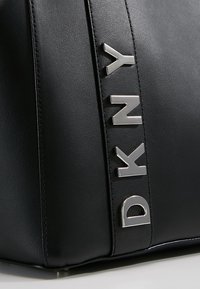 Czarna skórzana torebka z metalowym logo DKNY w kolorze srebrnym. Gładka tekstura z wyraźnym designem i widocznymi detalami szycia.