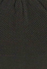 Beanie lavorato a maglia di colore grigio scuro, caratterizzato da un motivo testurizzato con una fascia a coste. Tessuto morbido con una finitura elasticizzata, adatto per le giornate fredde.