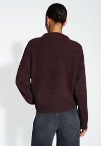 Pull bordeaux avec un design tricoté texturé, présentant un large col et une coupe décontractée, associé à un jean gris foncé.