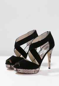 Zwarte suède hakken met kruislingse banden, open tenen en een getextureerd slangenprint platform. Voorzien van een stilettohak en binnenvoering.