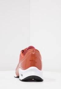 Nike Air sneaker featuring a red mesh upper, shiny red accents, white midsole, and black outsole. Textured finish with logo detail on heel.