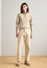 Pulover bej tricotat cu guler cu fermoar, asociat cu pantaloni bej largi și botine bej. Design simplu, texturat, fără modele.