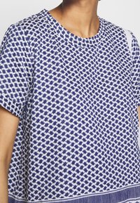 Kortärmad blå och vit mönstrad topp med rund hals, med en strukturerad stickad design och rak nederkant.