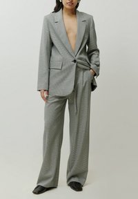 Grijze geruite blazer met notch-lapels en enkele knoopsluiting, gecombineerd met losse, bijpassende broek; gladde stoftextuur.