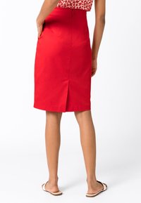 Punainen kynähame, joka on valmistettu sileästä kankaasta, takana halkio liikkumista varten, korkea vyötärö ja huomaamattomat taskut. Yhdistetty tasapohjaisten sandaalien kanssa.