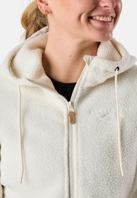 Weißer Fleece-Jacke mit Kapuze, ausgestattet mit einem durchgehenden Reißverschluss und Kordeln. Strukturierter Stoff und Lederakzent am Reißverschluss-Zipper.