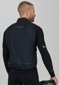 Schwarze Radweste mit einem Reißverschlusstasche, leichtem Stoff, Netzakzenten und einem Herzschlaglinien-Graphic auf dem Rücken. Enganliegendes Design.